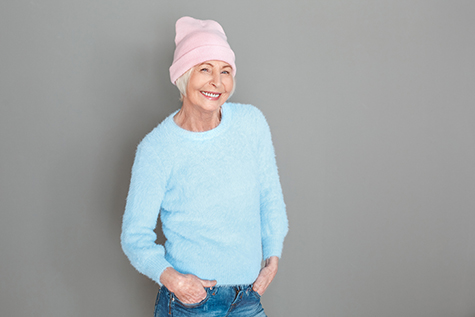 Senior woman in sweater and hat studio isolated on grey wall posing happy