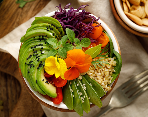Buddha bowl of mixed vegetables, quinoa and edible flowers, top view.