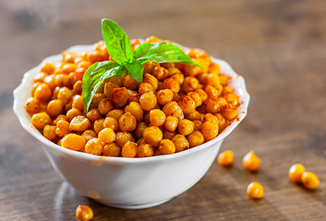 Fried spicy chickpeas in white bowl on wooden table background
