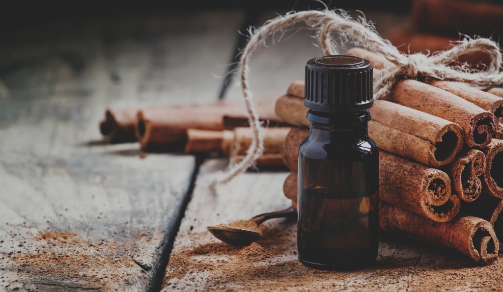 Essential cinnamon oil in a small bottle, ground cinnamon and cinnamon sticks on old wooden background, selective focus and toned image