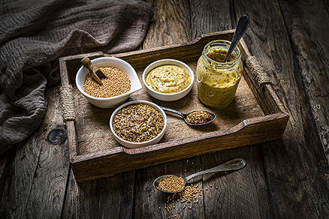 Dried mustard seeds, whole grain and Dijon mustard shot on rustic wooden table.