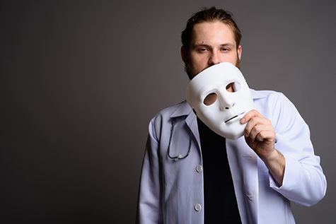 Portrait of bearded young man doctor holding white mask