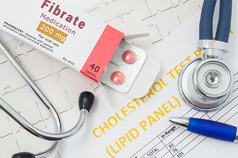 Fibrate drug for cholesterol lowering therapy concept photo. Open packaging with medication tablets, on which written "Fibrate", lies near stethoscope, result analysis on cholesterol (lipid panel)