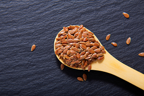 Close up Organic Flax seeds in wooden spoon on black slate stone plate