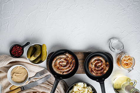 Wurst or Bratwurst with Fermented Cabbage, Pickled Cucumbers, and Spices in cast iron frying pan, on white background, top view flat lay , with space for text copyspace