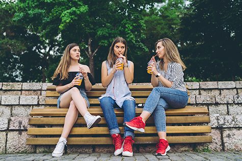 Three girlfriends drinking orange juice on a bench