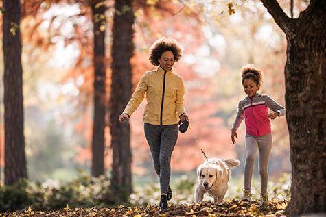 Happy African American mother and daughter running with golden retriever in the park.