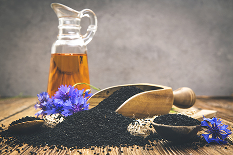 Black cumin seeds essential oil with wooden spoon and shovel on wooden background