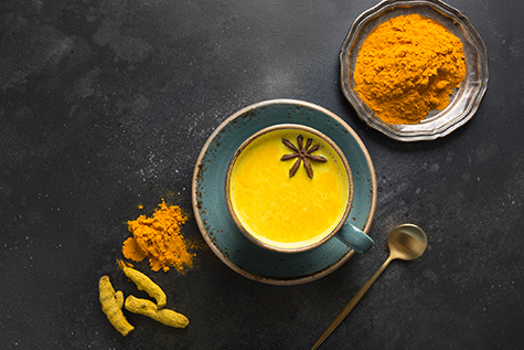 Cup of ayurvedic golden turmeric milk with curcuma powder and anise star on black. View from above.