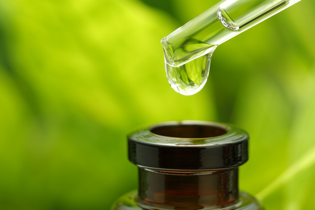 Droplet of herbal essence hovering over neck of small bottle