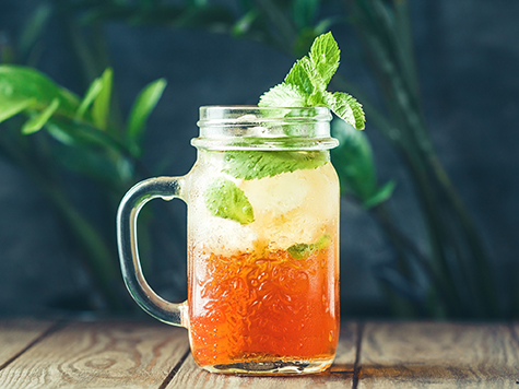Ice black tea in a glass jar with fresh mint on a wooden table.