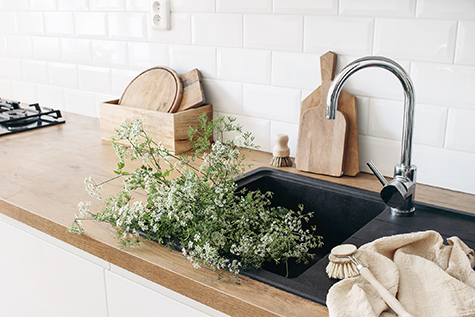 Closeup of kitchen interior. White brick wall, metro tiles, wooden countertops with chopping boards. Cow parsley plants in black sink. Modern scandinavian design. Home staging, cleaning concept.