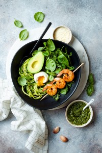 Buddha bowl with soft boiled egg, avocado, greens, zucchini noodles, grilled shrimps and pesto sauce. Vegetarian vegetable low carb lunch bowl.