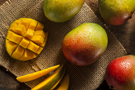 An image of ripe mangos with one cut open on a burlap mat