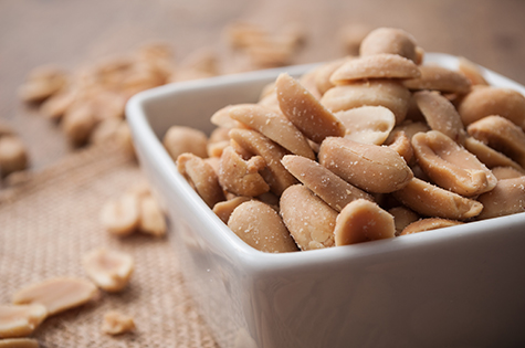salted peanuts in a porcelain bowl on wooden background