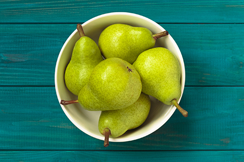 green pears in white bowl on blue wooden background.