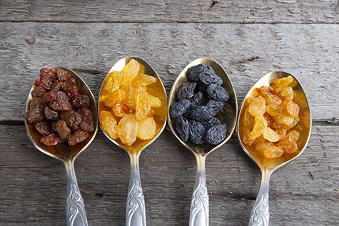 Raisins in metal spoons on wooden table