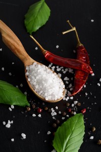 White sea salt in a wooden purse, with chili, spices and basil leaves on a black stone background