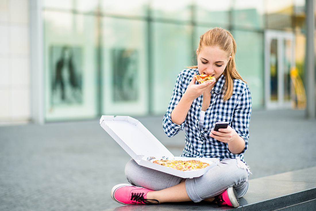 Teenager eating pizza looking in phone
