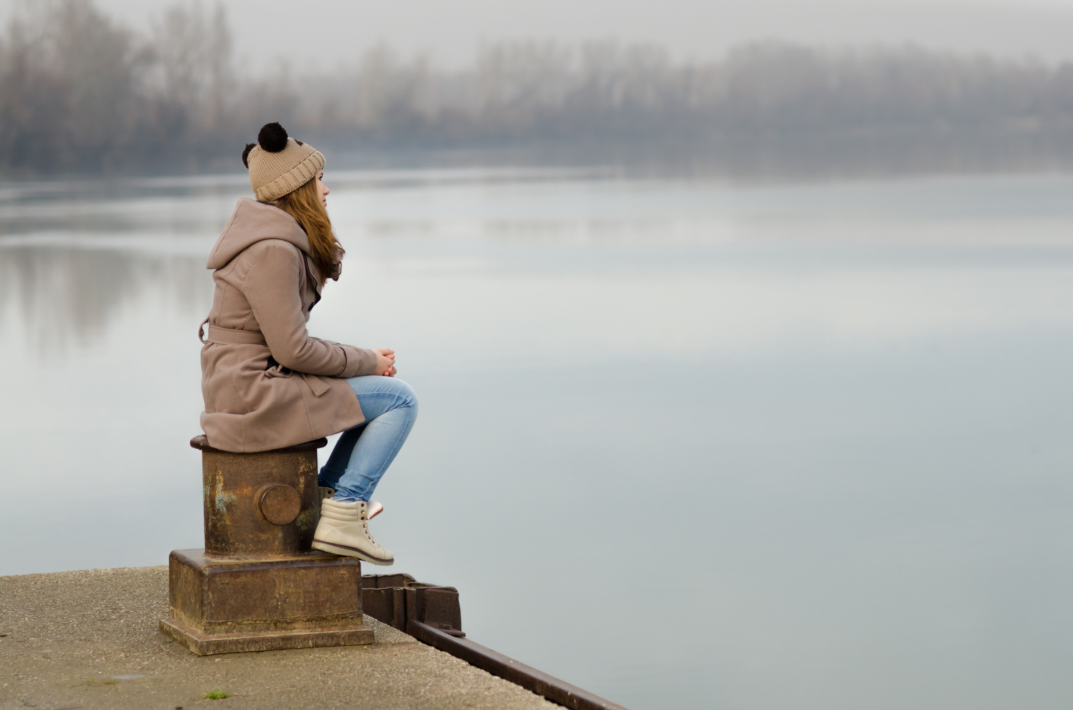 Lonely sad girl sitting on dock in winter