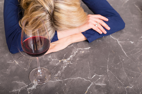 Depressed woman with wine glass resting her head on counter