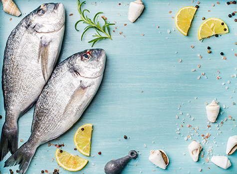 Fresh raw sea bream fish decorated with lemon slices, herbs and  shells on blue wooden background, copy spac