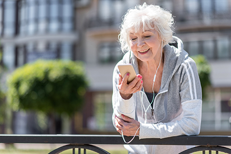 Cheerful old sporty woman listening to music via headphones