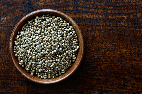 Hemp seeds in dark wooden bowl isolated on dark brown wood from above.