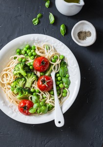 Veggie pasta. Vegetarian lunch - spaghetti with broccoli cabbage, green peas and cherry tomatoes on dark background, top view. Healthy food concept