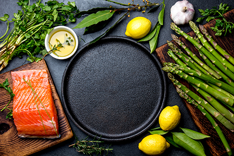 Raw salmon fillet, asparagus, lemons and herbs around cast iron plate. Food cooking background with copy space. Top view.